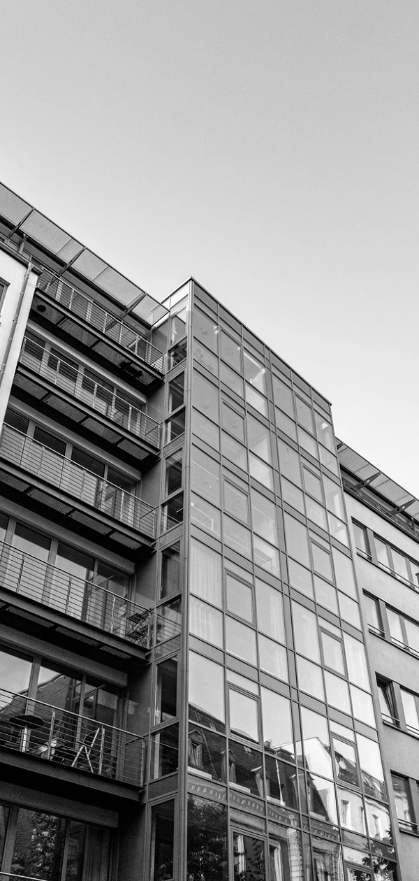 Moderne Wohngebäude mit großen Glasfenstern und Balkonen, umgeben von Bäumen, vor einem klaren blauen Himmel.