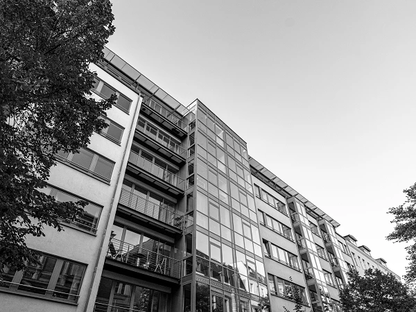 Die Aufnahme zeigt die Fassade eines modernen Hochhauses aus Glas, die hellblauem Himmel zugewandt ist, mit vielen Fenstern, die die Umgebung reflektieren.