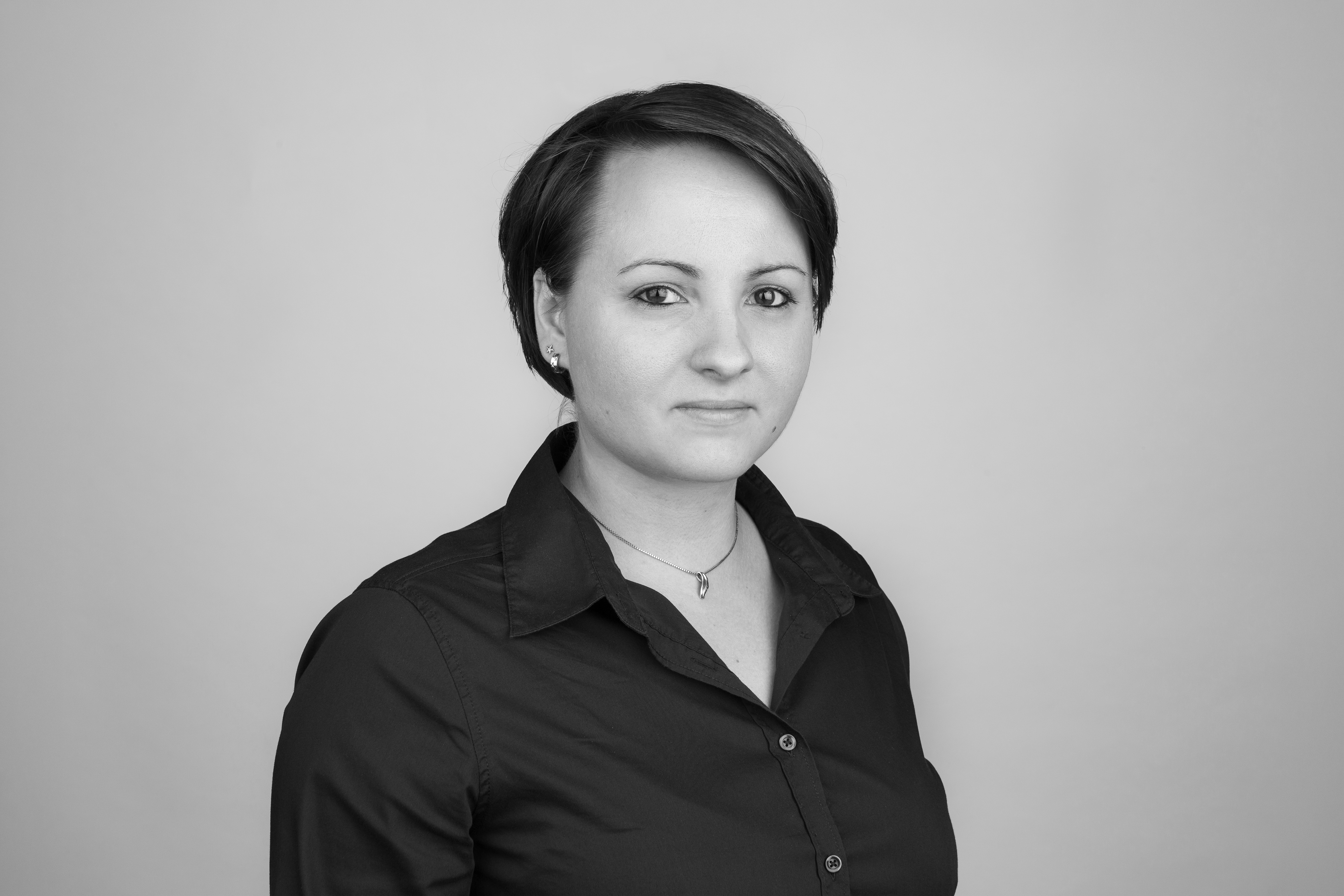 Eine Person mit kurzen, dunklen Haaren trägt ein blaues Hemd und schaut ernst in die Kamera, vor einem hellen Hintergrund.